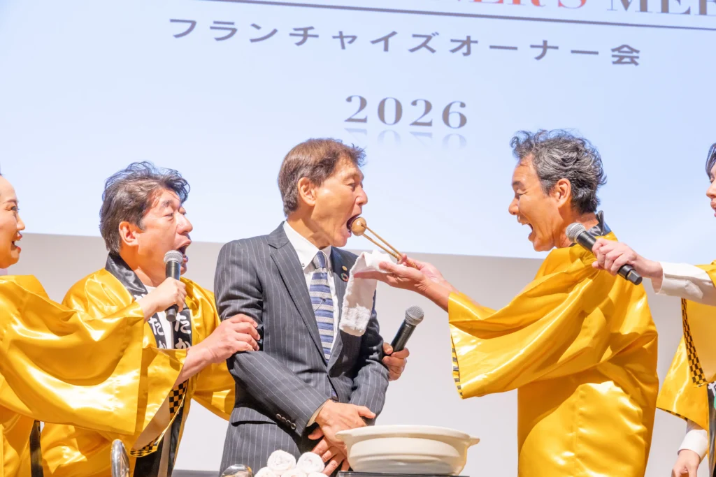 ［画像：熱々おでん芸に挑戦する渡辺会長］